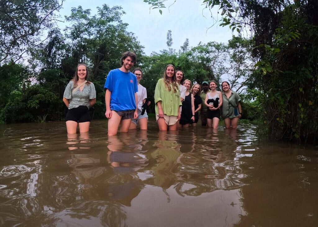 A group of people standing in shallow water surrounded by dense foliage.