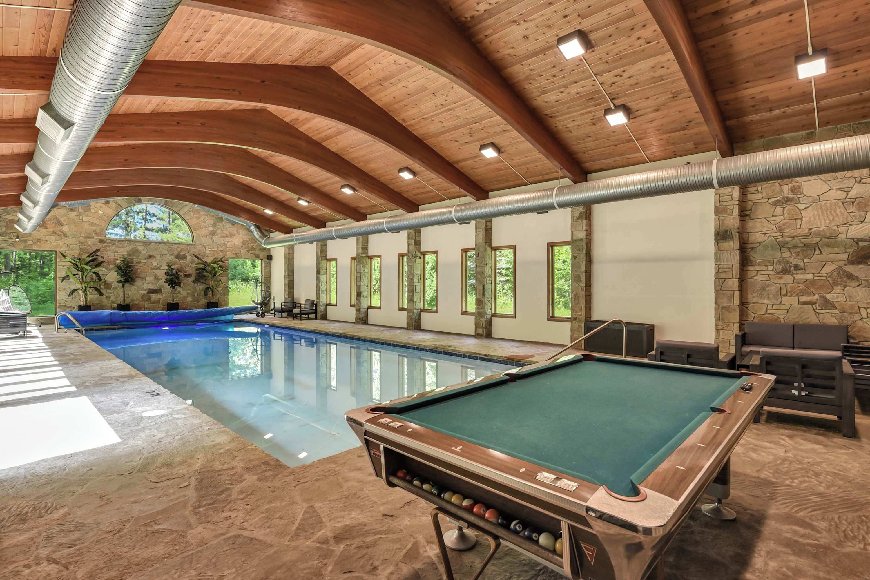 Uma área interna com piscina, mesa de bilhar, paredes de pedra e vigas de madeira.