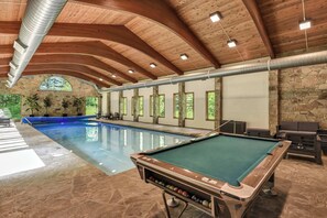 Un espace piscine intérieur doté d’une table de billard, de murs en pierre et de poutres en bois.
