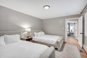 Een moderne hotelkamer met twee bedden, een nachtkastje, een lamp en een gang die naar een andere kamer leidt.