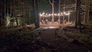 A forested area with string lights and outdoor seating.