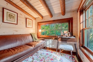 L’intérieur d’un chalet en bois est aménagé avec un canapé en cuir, un bureau avec une chaise, des tableaux encadrés accrochés au mur et une fenêtre donnant sur un paysage verdoyant.
