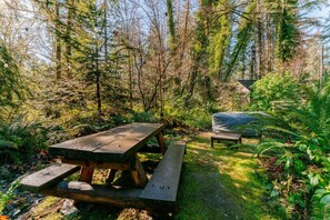 A picnic table in a forested area with a bench and a covered object nearby. - Creekside Fairytale Cabin Near Ferries to Seattle (Port Orchard)