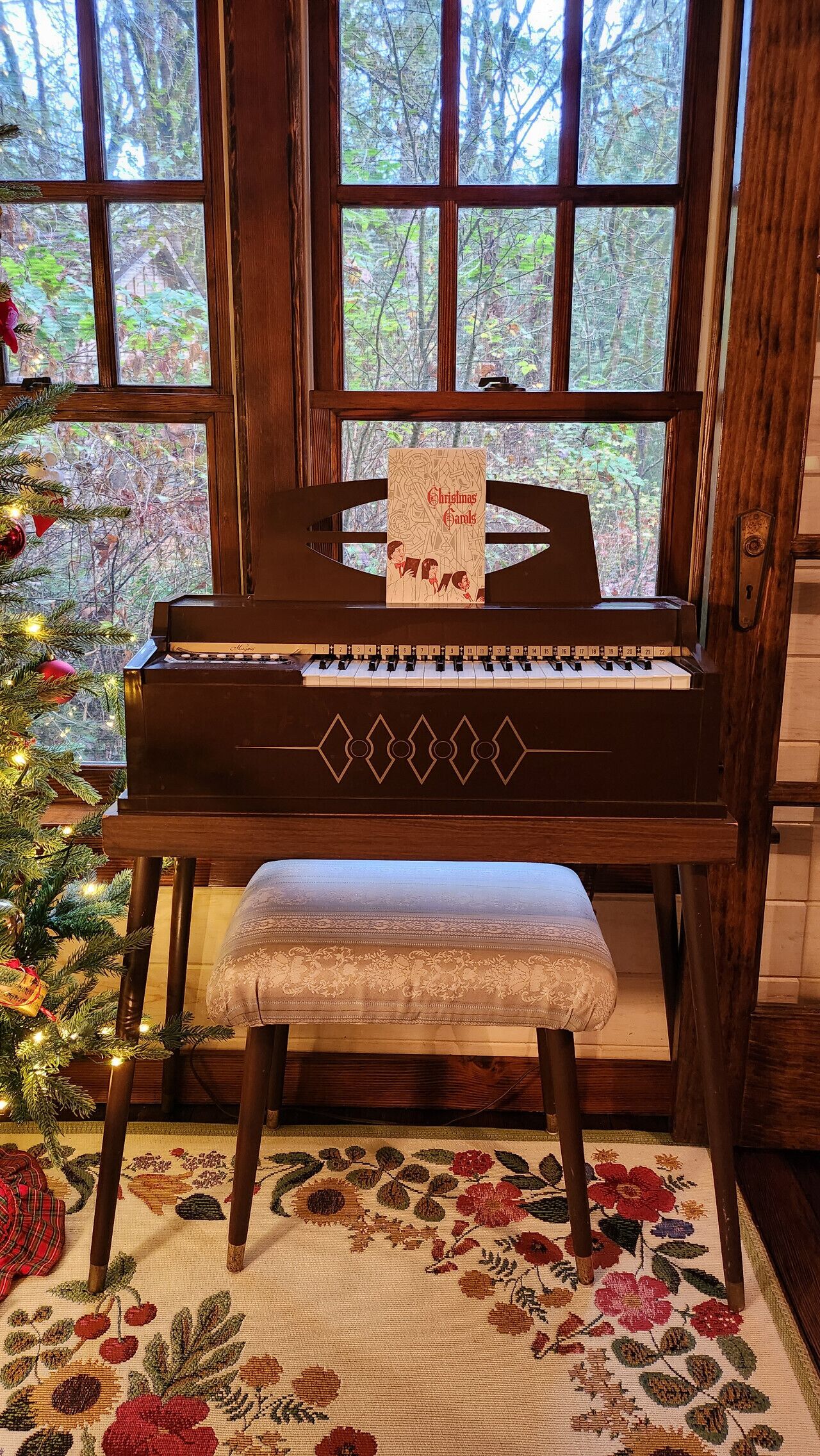 Un piano de cola con una tarjeta navideña frente a una ventana que da a un bosque.