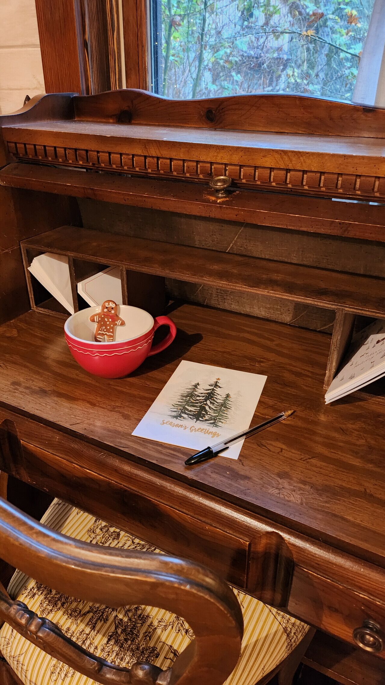 A wooden desk with a red bowl, a gingerbread man, a pen, and a Christmas card.