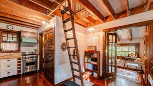 Interieur van een houten blokhut met een keuken, een ladder, een boekenkast en een piano.