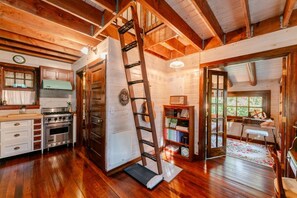 L’intérieur d’une cabane en bois comprenant une cuisine, une échelle, une bibliothèque et un piano.