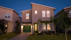 Una moderna casa a due piani con un garage color verde, un piccolo giardino anteriore con palme e un vialetto lastricato.