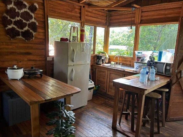 Una cabaña rústica de madera con una zona de cocina que incluye un refrigerador, un lavamanos y mesas de madera.
