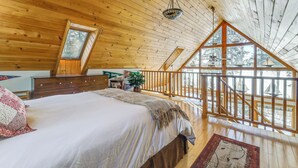 A bedroom with a large bed, wooden ceiling, a window, and a balcony with a railing. - Gateway to Acadia! Green Lake Home w/ Hot Tub (Dedham)