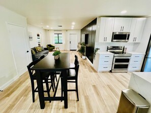 A modern kitchen with white cabinets, stainless steel appliances, and a dining area with a black table and chairs. - Kokomo Beach House!  2-bedroom home <1 mile to downtown & 2 miles to the beach! (Lake Worth Beach)