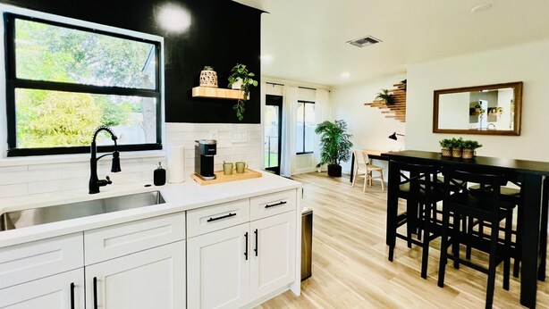 Una cocina moderna con armarios blancos, salpicadero negro y ventana con vistas a la vegetación.