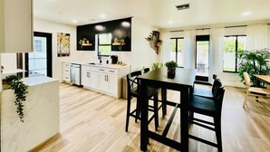 Una cocina moderna con armarios blancos, encimera negra y comedor con mesa y sillas de madera.