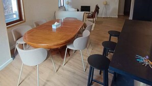 Een ruime kamer met een houten eettafel omringd door stoelen, een donkere bar en een televisie op een standaard.