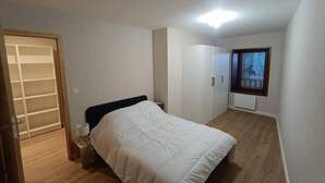Een slaapkamer met een bed, een kast, een klein tafeltje met lamp, een raam met uitzicht en een plafondlamp.