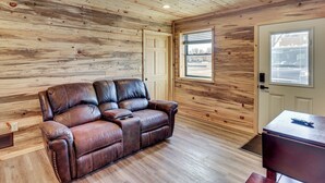 A wooden-paneled room with a leather sofa, a small table, and a window with blinds.