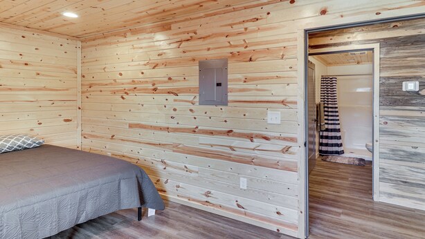 A wooden-paneled room with a bed, a door leading to a bathroom, and a power outlet on the wall.