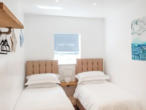 Ein kleiner, hell eingerichteter Raum mit zwei Betten, einem Fenster mit Meerblick und einem Bild an der Wand.