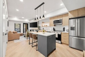 A modern kitchen with a central island, stainless steel appliances, and a dining area with a sofa and chairs. - Charming Mountain Escape1BR w/ Balcony Near Banff (Canmore)