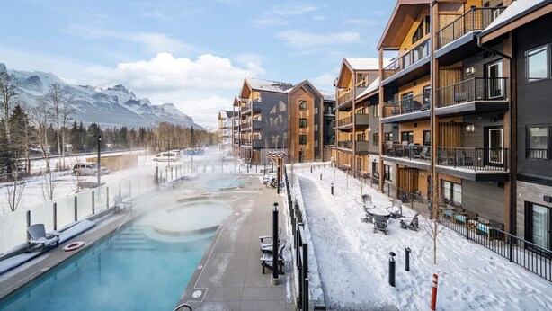 Un hotel moderno con numerosi balconi, una piscina e vista sulle montagne innevate.