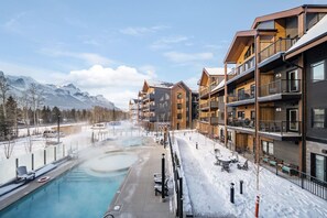 A modern hotel with multiple balconies, a pool, and a view of snow-covered mountains. - Charming Mountain Escape1BR w/ Balcony Near Banff (Canmore)