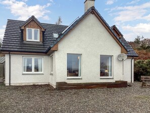 A house with a gabled roof, two windows, a satellite dish, and a gravel driveway. - 4 bedroom accommodation in Drumnadrochit (Drunmnadrochit)