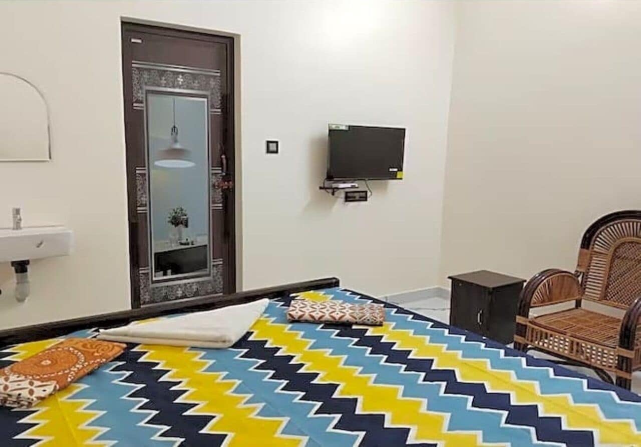 Un dormitori amb un llit, televisió, mirall, porta i una cadira.