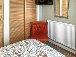 Ein Zimmer mit einem Bett, einem roten Sessel, einem Kleiderschrank, einer Heizung und einem Fernseher an der Wand.