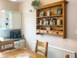 A kitchen with wooden cabinets, a built-in shelf with decorative items, a dining table with chairs, and a radiator below. - 3 bedroom accommodation in Cullen, near Buckie (Buckie)