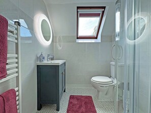 A bathroom with a toilet, a sink with a mirror, a towel rack, and a shower area. - 3 bedroom accommodation in Cullen, near Buckie (Buckie)
