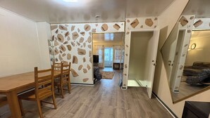 A room with a wooden dining table and chairs, a stone-patterned wall, and a view into another room with a sofa and curtains. - N2  north philadelphia , quiet one room shared house  (Philadelphia)