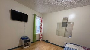 A bedroom with a bed, a TV mounted on the wall, a window with curtains, and a mirror. - N2  north philadelphia , quiet one room shared house  (Philadelphia)
