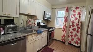 A kitchen with white cabinets, a microwave, a stove, a toaster, and a window with floral curtains. - N2  north philadelphia , quiet one room shared house  (Philadelphia)