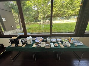 A table set with various dishes and utensils, a portable coffee maker, and a chair, with a view of a grassy area and trees through large windows. - Daido Garden Hotel Yunoyama SPA Resort (Komono)