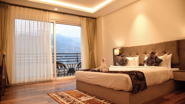 Quarto de hotel moderno com uma cama grande, varanda e vista, e teto bem iluminado.