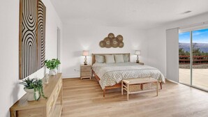 A bedroom with a large bed, bedside tables, a bench, and a view of the outdoors. - Yosemite/Bass Lake Villa+HotTub EVcharger (Oakhurst)