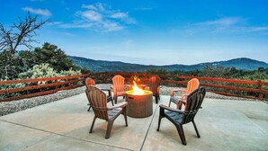 An outdoor seating area with a fire pit and chairs, surrounded by a wooden fence and a scenic view of hills. - Yosemite/Bass Lake Villa+HotTub EVcharger (Oakhurst)