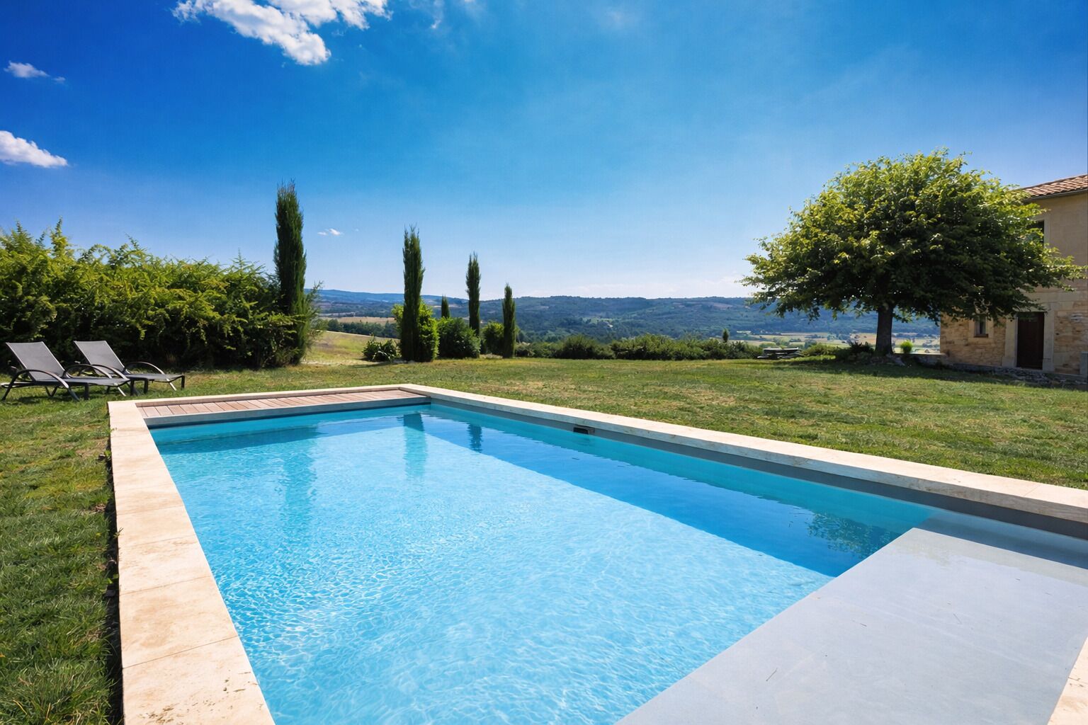 A rectangular swimming pool with a clear blue water surface, surrounded by a grassy lawn and a stone wall.
