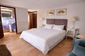 Un dormitorio con una cama grande, dos mesitas de noche con lámparas, un armario de madera, un baño con lavamanos y espejo, y dos elementos decorativos en la pared.