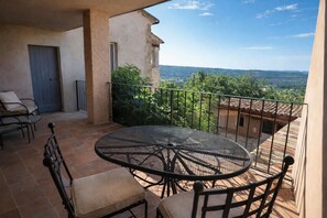Un balcón con una mesa redonda y sillas, una puerta, y vistas a un paisaje montañoso.