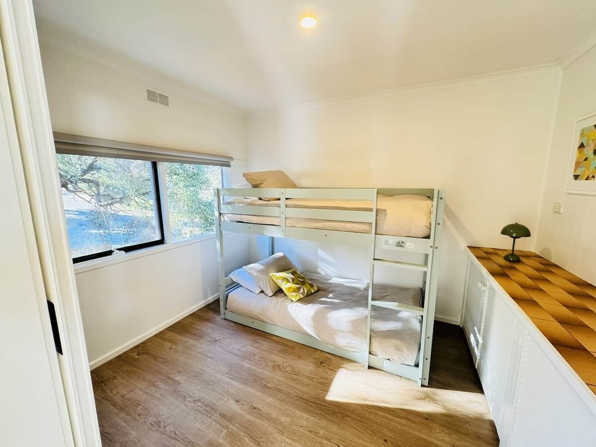 A bunk bed room with a window, a desk, and a lamp.