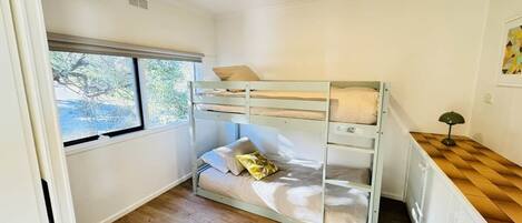A bunk bed room with a window, a desk, and a lamp.