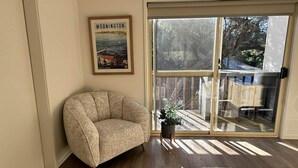 Et værelse med en beige lænestol, et billede i ramme af Mornington, og en skydedør, der fører ud til en terrasse.