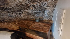 Een eenvoudige kamer met een houten tafel, een metalen emmer en een bed met een wit laken.
