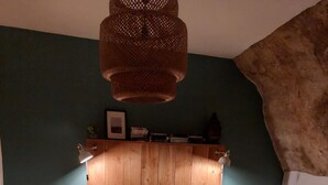 Een slaapkamer met een houten hoofdbord, twee nachtkastjes, een bed met een grijsgroene spreidek en een hanglamp.