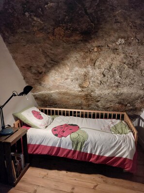 Ein Schlafzimmer mit rustikalem Stein-Gewölbe, einem hölzernen Bett mit floralem Überwurf und einer Nachttischlampe.