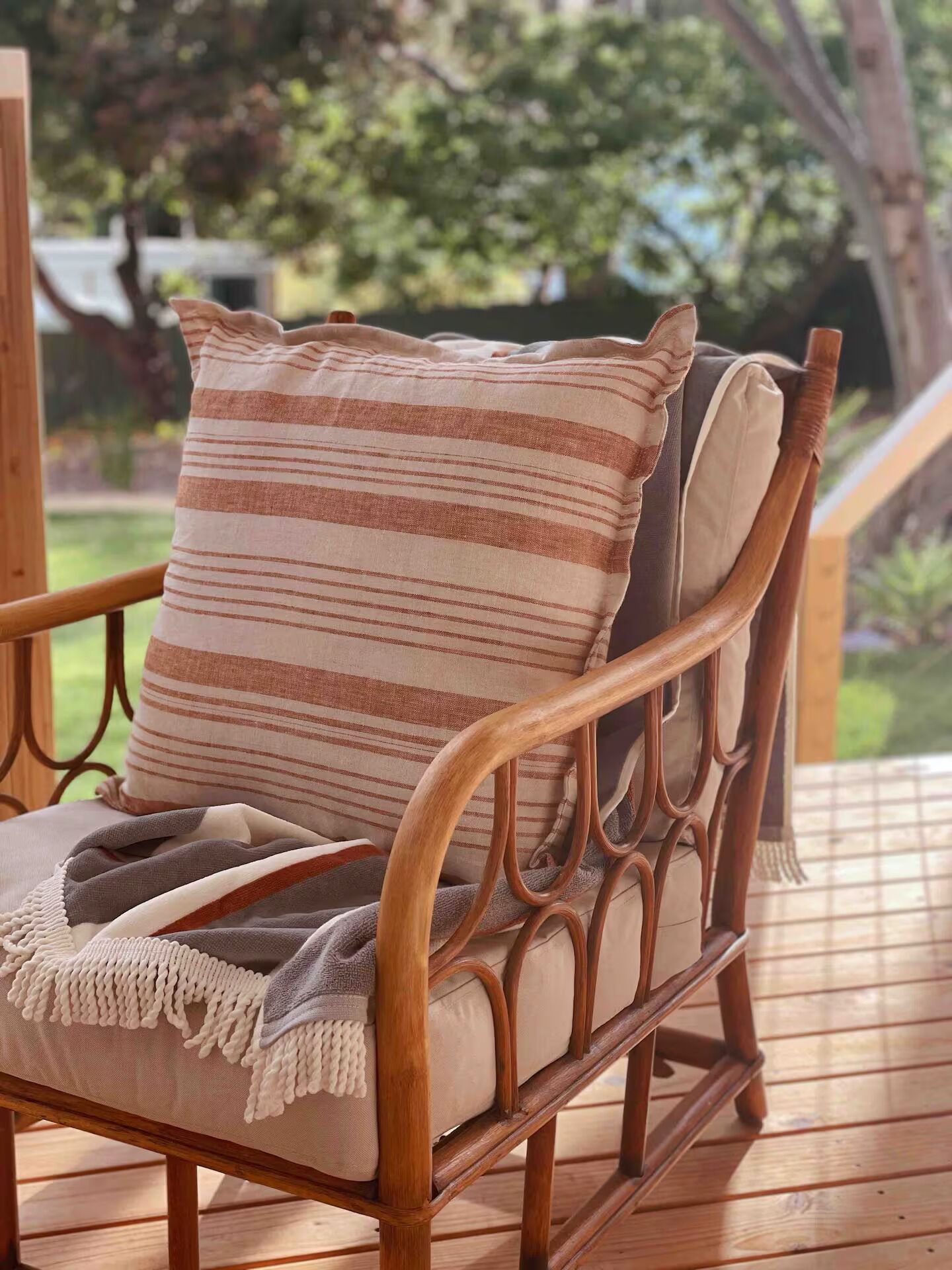 A wicker chair with a striped cushion and a fringed throw blanket on a wooden deck.