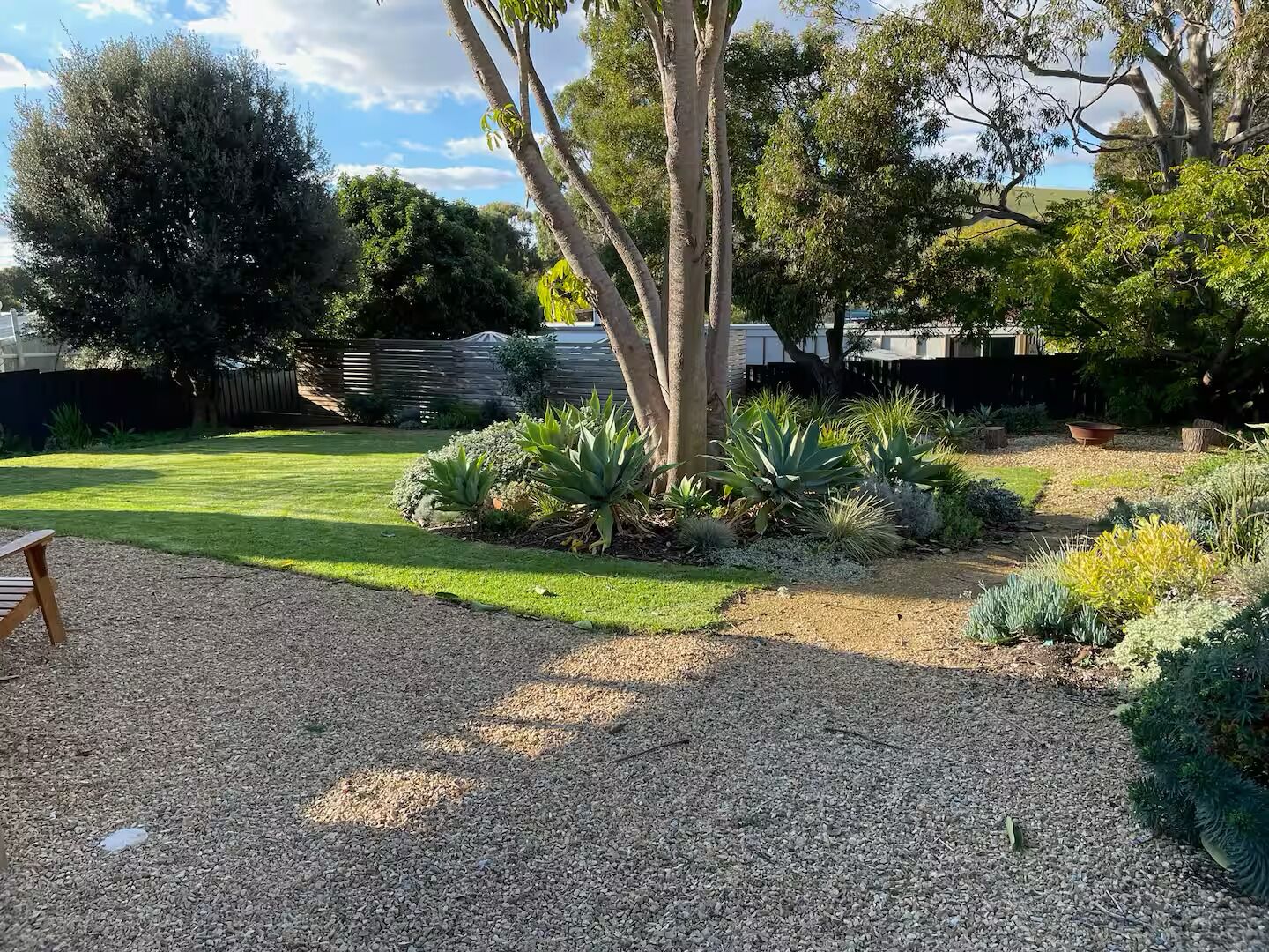 A well-maintained garden with a variety of plants, a gravel path, and a wooden bench.