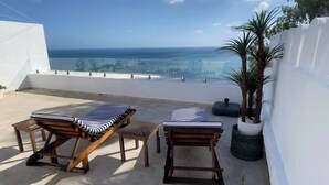 Eine Dachterrasse mit zwei Holzliegen und einem kleinen Tisch, mit Blick auf die Küste.