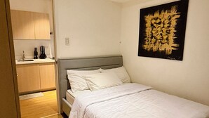 Ein Schlafzimmer mit Bett, einem Bild an der Wand und einem durch eine offene Tür einsehbarer Küchenbereich.